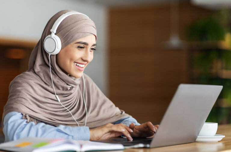 A woman studying the Quran online with headphones and a laptop